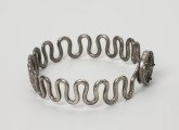 Bransoleta wężykowata - ujęcie z boku; Bransoleta srebrna wężykowata z okrągłym zapięciem kapsułkowym z lutowanej blachy. Kabłąk z kolei tworzy srebrny drut o średnicy 2 mm wygięty w gęsty esowaty zygzak.