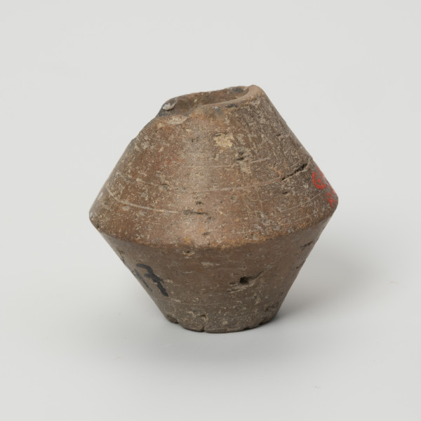 Przęślik dwustożkowy - ujęcie z boku; Przęślik gliniany dwustożkowy o ściętych, płaskich biegunach, dobrze wypalony, o barwie jasnobrązowej. Na powierzchni widoczne ślady toczenia oraz miejscami ubytki gliny. Wzdłuż osi pionowej przęślika znajduje się otwór o średnicy ok. 0,8 cm. Jeden z biegunów nieznacznie uszkodzony.