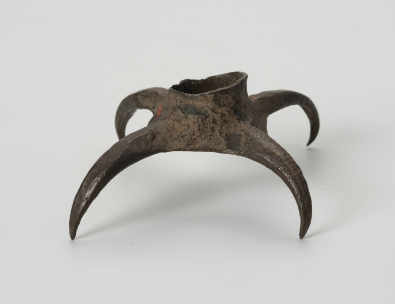 Pobocznica wędzidła końskiego (krępulec) - ujęcie z boku; Krępulec tzw. kolczasty złożony jest z niewielkiej tulejki zaopatrzonej w cztery kolczaste ramiona lekko zagięte do środka. Przedmiot wykonany jest z brązu.