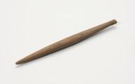 Wrzeciono - ujęcie z boku; Podłużne, smukłe wrzeciono wykonane z drewna. Jest okrągłe w przekroju, zwężające się ku końcom.