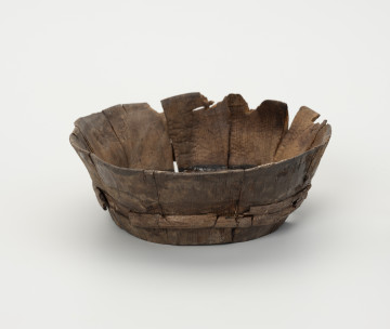 Miska klepkowa - ujęcie z przodu; Miska klepkowa zachowana w całości, nieco uszkodzona i zdeformowana, zakonserwowana, zbudowana z wielu elementów: dna, 10 klepek oraz obręczy spajającej klepki złożonej z podwójnego zwoju łyka. Dno koliste, ze ściętą ukośnie krawędzią, umieszczoną w wyciętych specjalnie w dolnej części wewnętrznych stron klepek, otworach, zwanych wątorami. Klepki spojone zostały obręczą z łyka, umieszczoną w zagłębieniach wyciętych w zewnętrznych ich stronach.