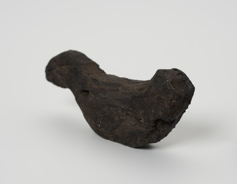 Ptaszek z kory - ujęcie z przodu; Figurka ptaszka wystrugana z kory o schematycznej sylwetce. Wyodrębniona została jedynie głowa i ogon bez pozostałych typowych cech ptasich. Powierzchnia wykończona starannie, bez zadziorów.