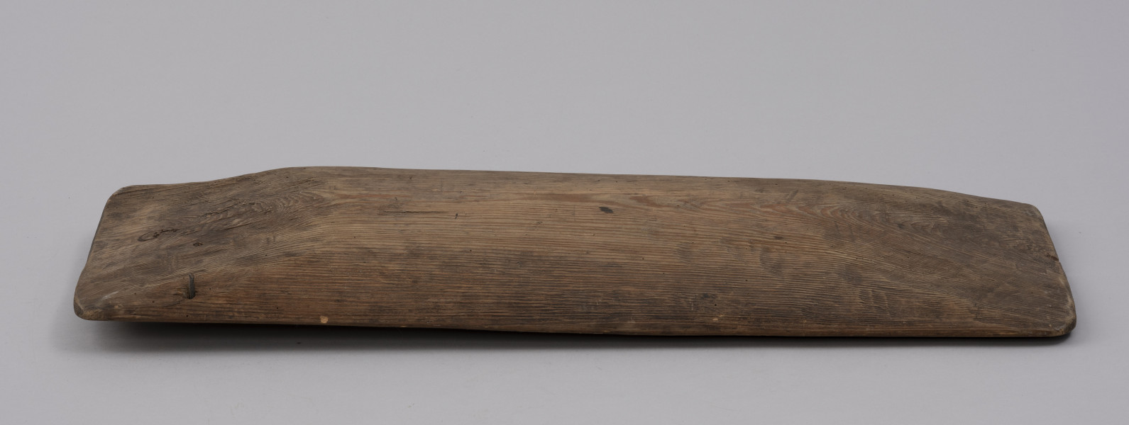 tacka do sznurów haczykowych - ujęcie z boku; Płytka, drewniana niecka, wykonana techniką stolarską z jednego kawałka drewna. Naroża lekko zaokrąglone. Na jednym z końców niecki, przy krawędziach dłuższych boków, widoczny otwór, przez który przechodzi drut, służący do mocowania haczyków.