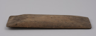 tacka do sznurów haczykowych - ujęcie z boku; Płytka, drewniana niecka, wykonana techniką stolarską z jednego kawałka drewna. Naroża lekko zaokrąglone. Na jednym z końców niecki, przy krawędziach dłuższych boków, widoczny otwór, przez który przechodzi drut, służący do mocowania haczyków.