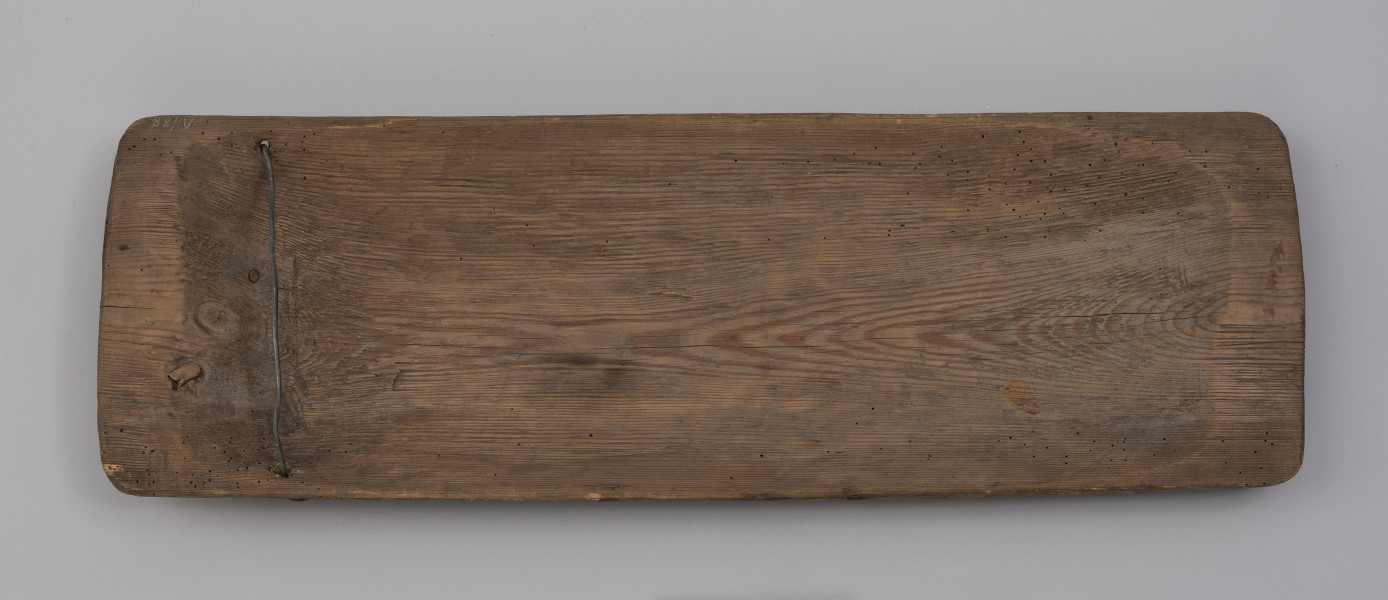 tacka do sznurów haczykowych - ujęcie z góry; Płytka, drewniana niecka, wykonana techniką stolarską z jednego kawałka drewna. Naroża lekko zaokrąglone. Na jednym z końców niecki, przy krawędziach dłuższych boków, po jednym otworze, przez który przechodzi drut, służący do mocowania haczyków. Widoczne ślady użytkowania.