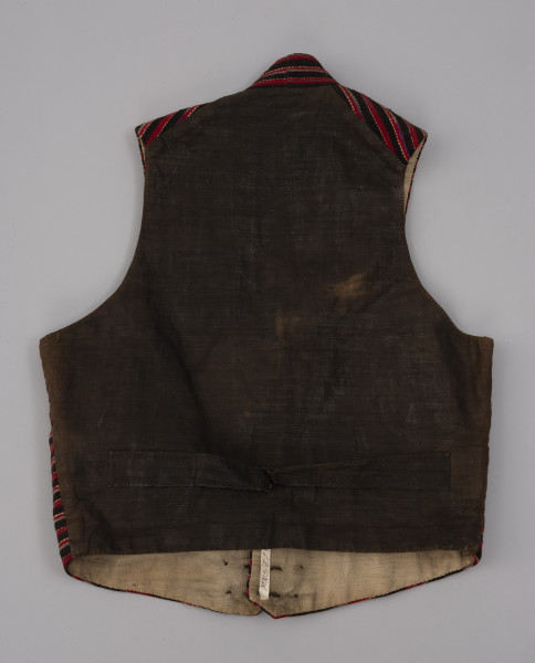 Kamizelka męska - ujęcie z tyłu; Kamizelka część męskiego stroju z półwyspu Mönchgut na Rugii/Niemcy. Plecy uszyte z tkaniny płóciennej prawdopodobnie pierwotnie w kolorze czarnym ( obecnie wyblakłym ) z charakterystycznym dla fasonu kamizelek paskiem regulującym. Podszewka z białego lnianego płótna wykonanego na krosnach tkackich splotem płóciennym prostym.