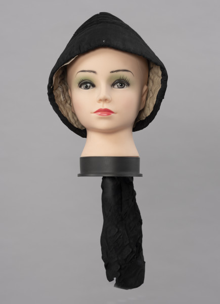 Czepek damski - ujęcie z przodu; Czepek damski, codzienny. Wykonany z tkanin produkcji fabrycznej (wełna, atłas) i białego, lnianego płótna wykonanego na krosnach tkackich splotem płóciennym prostym. Główka czepca  z tkaniny wełnianej, czarnej, wokół główki naszyta czarna atłasowa tkanina. Czepek zszyty z dwóch kawałków, szew wzdłuż pionowej linii głowy, ściągany nad karkiem nicią. Główka wyraźnie zaokrąglona, zachodząca wyraźnie na uszy. Od środka czepek podbity lnianym, białym płótnem i wypełniony grubym usztywniającym materiałem. Przez wszystkie warstwy tkanin przechodzą w wielu miejscach przeszycia białymi i czarnymi nićmi tworzącymi ich złączenie  jako przepikowanie tkaniny.  

Literatura: 