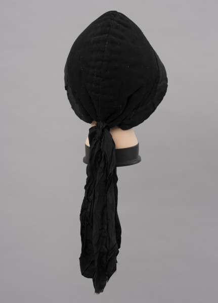 Czepek damski - ujęcie z tyłu; Czepek damski, codzienny. Wykonany z tkanin produkcji fabrycznej (wełna, atłas) i białego, lnianego płótna wykonanego na krosnach tkackich splotem płóciennym prostym. Główka czepca  z tkaniny wełnianej, czarnej, wokół główki naszyta czarna atłasowa tkanina. Z tyłu dekoracyjna kokarda z atłasowej wstążki. Czepek zszyty z dwóch kawałków, szew wzdłuż pionowej linii głowy, ściągany nad karkiem nicią. Główka wyraźnie zaokrąglona, zachodząca wyraźnie na uszy. Od środka czepek podbity lnianym, białym płótnem i wypełniony grubym usztywniającym materiałem. Przez wszystkie warstwy tkanin przechodzą w wielu miejscach przeszycia białymi i czarnymi nićmi tworzącymi ich złączenie  jako przepikowanie tkaniny.  

Literatura: 