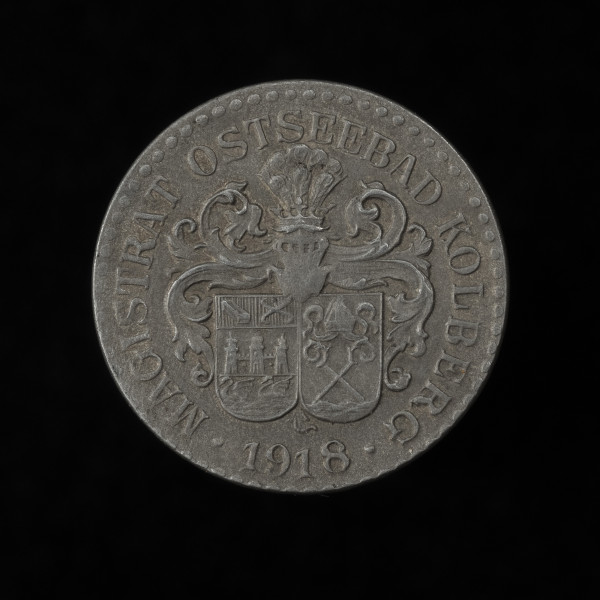 10 fenigów - awers; Okrągła moneta o gładkim rancie. Awers: w polu dwutarczowy herb Kołobrzegu pod hełmem z klejnotem i labrami; lewa tarcza, podzielona jest na trzy pasy; na pierwszym panew i haki, na drugim mur miejski z trzema basztami, na trzecim płynące łabędzie; na prawej tarczy pod mitrą, a nad falami, skrzyżowane pastorały – symbol zwierzchności biskupów kamieńskich nad miastem; pod herbem, między dwoma punktami data: 1918; w otoku napis MAGISTRAT OSTSEEBAD KOLBERG; obwódka perełkowa.