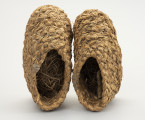 Buty słomniane - ujęcie z góry; Buty wykonane ze słomy (prawdopodobnie żytniej) techniką spiralną, wyrób plecionkarski, jednostkowy. Podeszwa płaska, stopa w całości zabudowana, cholewka otwarta. Wykonane z warkocza plecionego z powróseł słomianych różnej grubości, początek zawiązuje się słomą lub sznurkiem i plecie się rękoma warkocz, dokładając co pewien czas nowe pasmo słomy. Poszczególne rzędy, z których wypleciono buty powiązane są ze sobą za pomocą sznurka.