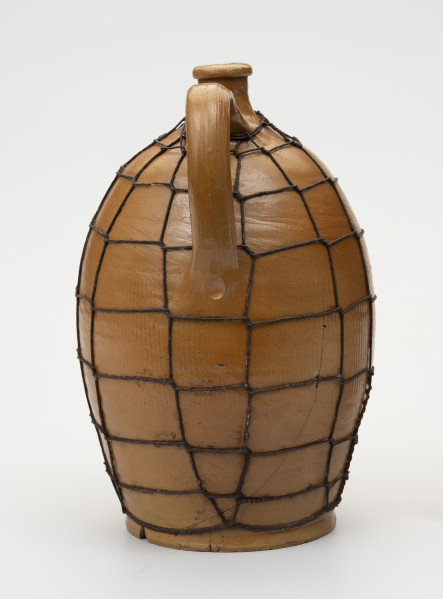 Butla z odrutowaniem - ujęcie z drugiego boku; Kamionkowa butla o owalnym kształcie i wyraźnie wyodrębnionym dnie. Brzusiec w dolnej części wyraźnie węższy, o największym rozchyleniu powyżej połowy wysokości, w górnej partii przechodzi bezpośrednio w szyjkę. Szyjka krótka, wąska, wyraźnie wyodrębniona z pogrubionym wylewem. Ucho taśmowe, esowato wygięte z górnym punktem zaczepienia nieco poniżej miejsca przejścia brzuśca w szyjkę i dolnym - powyżej połowy wysokości naczynia. W miejscu przejścia ucha w brzusiec wyciśnięta, prawdopodobnie palcem, kropka. Glazura szyjki na zewnątrz brązowa. Butla odrutowana cienkim drutem dla wzmocnienia uszkodzonego naczynia. Pęknięcie biegnie prawie przez całą wysokość brzuśca i łukowato do krawędzi dna.