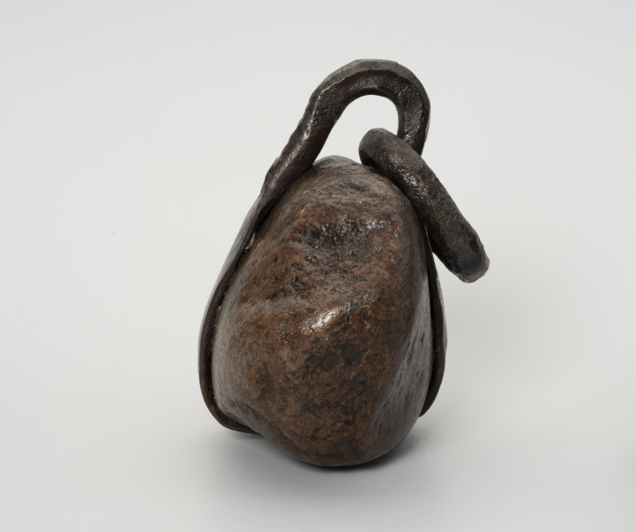 Ciężarek do sieci - ujęcie z boku; Ciężarek do obciążania sieci wykonany z kamienia. W środkowej części kamień otoczony wykutym z żelaza, spłaszczonym pierścieniem. W części górnej pierścień wystaje poza obręb kamienia tworząc pętlę, przez którą przechodzi owalne, żelazne ogniwo, służące przymocowaniu ciężarka do sieci.