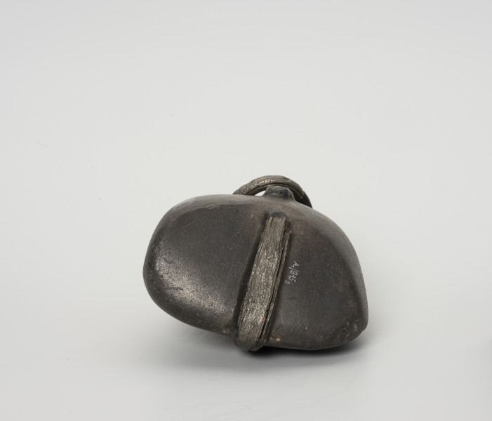 Ciężarek do sieci - ujęcie z dołu; Ciężarek do obciążania sieci wykonany z szarego kamienia o gładkiej powierzchni. Kamień otoczony żelaznym, kutym pierścieniem, którego końce nie łączą się ze sobą (wtórne uszkodzenie metalu).