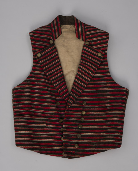 Kamizelka męska - ujęcie z przodu; Kamizelka część męskiego stroju z półwyspu Mönchgut na Rugii/Niemcy. Przód z tkaniny wełnianej, prawdopodobnie wykonanej na krosnach tkackich, wzór w wąskie paski ułożone na kamizelce poprzecznie w kolorach: czerwonym, szarym, brązowym i białym. Pod szyją wysoka stójka, klapy szeroko wyłożone zapinane na górze na mosiężne guziki. Zapięcie dwurzędowe na 7 mosiężnych guzików. Pod stójką, po obu jej stronach  po jednym mosiężnym guziku ( forma ozdoby). Na bokach małe wpuszczane kieszonki, dół zakończony prosto. Podszewka z białego lnianego płótna wykonanego na krosnach tkackich splotem płóciennym prostym.