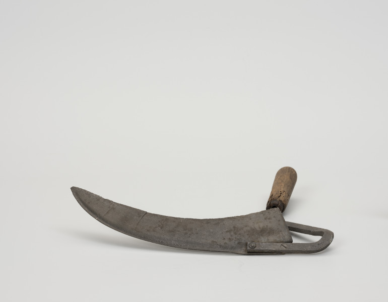 Półkosek - ujęcie z dołu; Półkosek składający się z żelaznego ostrza i drewnianego uchwytu  kształtem podobny jest do małej kosy. Żelazne, wydłużone ostrze zwężające się ku końcowi tworzy szpiczaste zakończenie, które osadzone jest na żelaznym, wygiętym skośnie kosisku przymocowanym za pomocą dwóch nitów do drewnianej, toczonej rękojeści, zakończonej bolcem.