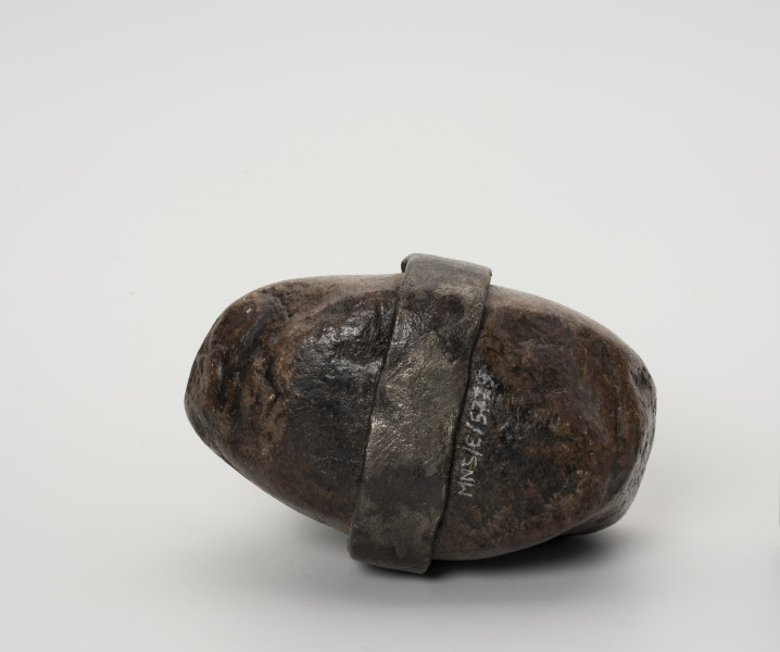 Ciężarek do sieci - ujęcie z dołu; Ciężarek do obciążania sieci wykonany z kamienia. W środkowej części kamień otoczony wykutym z żelaza, spłaszczonym pierścieniem.