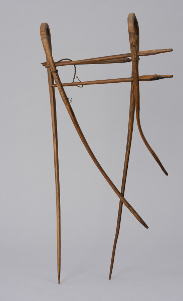 Grabki do kosy - ujęcie ze skosu; Grabki do kosy w postaci długich drewnianych zębów mocowanych do kosy, służących do lepszego układania się ścinanego zboża. Składają się z dwóch łukowato wygiętych prętów o nierównej długości. Po jednej stronie pręty biegną równolegle do siebie i zgodnie z kierunkiem nadanym przez wygięcie. Po drugiej stronie, gdzie konstrukcja wzmocniona jest dwoma poprzeczkami zamocowanymi prostopadle do prętów, których końce powyżej poprzeczek wygięte są w łagodny łuk. Dłuższe boki narzędzia mocowane są do trzonka kosy, krótsze do jej ostrza.