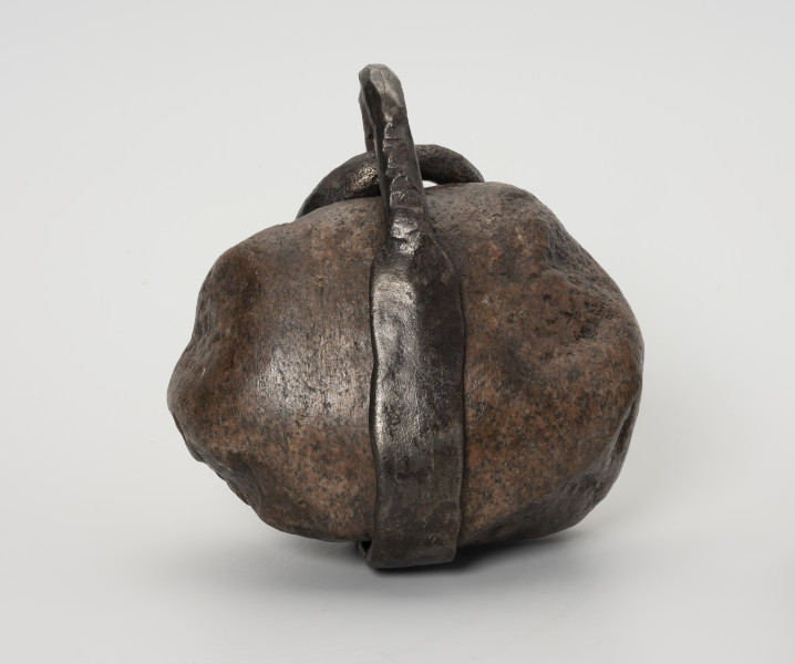 Ciężarek do sieci - ujęcie z tyłu; Ciężarek do obciążania sieci wykonany z kamienia. W środkowej części kamień otoczony wykutym z żelaza, spłaszczonym pierścieniem. W części górnej pierścień wystaje poza obręb kamienia.