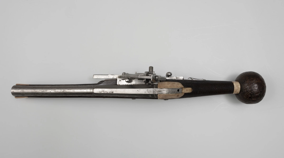 Puffer (pistolet z zamkiem kołowym) - ujęcie z góry; Lufa stalowa przy wylocie pogrubiona. W części dennej krótkie karbowania, przed nimi wybite litery H i R, a między nimi lew trzymający strzałę. Zamek wykonany ze stali. Z lewej strony blachy zamkowej bezpiecznik. Korba lekko pochylona, zakończona kolistą drewnianą głowicą.