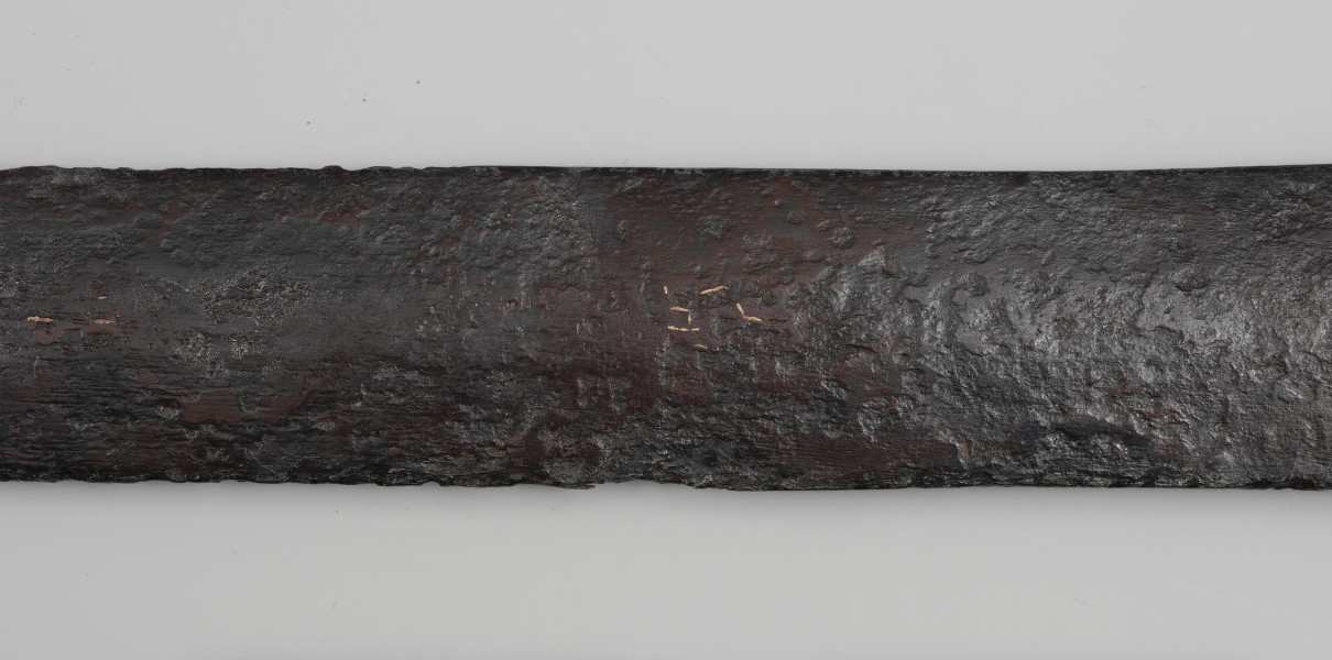 Miecz dwuręczny typu XVIII (Oakeshott) - detal; Ujęcie fragmentu głowni. Widoczne pozostałości po rytych znakach wypełnione żółtym metalem.