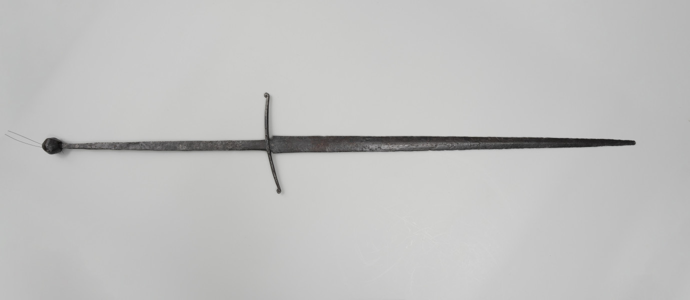 Miecz dwuręczny typu XVIII (Oakeshott) - ujęcie z tyłu; Miecz jest najbardziej zbliżony typem według typologii Oakeshotta do XVIIIb, T2, 1b. Głownia jest płaska, dwusieczna, lekko zbieżna ku sztychowi, a sam sztych centryczny. Trzpień jest długi (47,7 cm), przedłużony techniką skuwania i zwężający się ku końcowi. Jelec krzyżowy jest lekko wygięty ku głowni, z zawiniętymi do góry końcami. Nie zachowała się okładzina trzonu rękojeści.