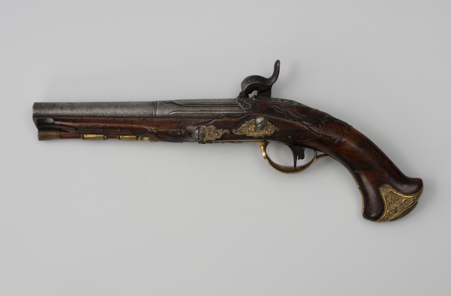Para pistoletów kapiszonowych - ujęcie z przodu; Pistolet kapiszonowy, pojedynkowy. Lufa stalowa okrągła, zakończona warkoczem zdobionym motywem roślinnym. Zamek kapiszonowy przerobiony ze skałkowych, zdobiony motywami roślinnymi. Zamek mocowany za pomocą dwóch śrub. Kontrblachy z motywami liści i kwiatów. Kabłąk ozdobiony rocaillowym wzorem. Kolba z drewna orzechowego. Łoża i rękojeść rzeźbiona w motywy rocaillowe. Pobojczyk i łoże u wylotu lufy zakończone kościanymi nakładkami. U spodu łoża dwie miedziane tulejki przytrzymujące pobojczyk. Głowica kolby jest spłaszczona, jej okucie jest mosiężne, zdobione motywem roślinnym.