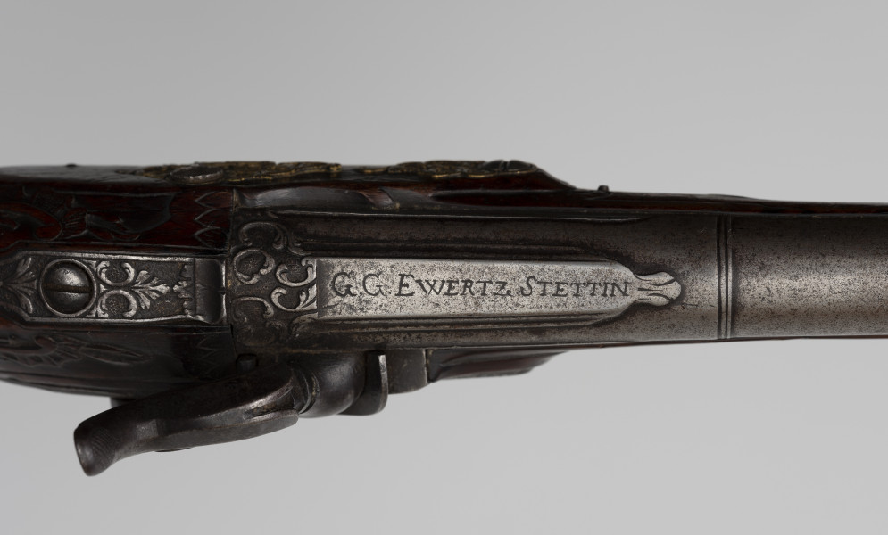 Para pistoletów kapiszonowych - detal; Fragment pistoletu kapiszonowego, pojedynkowego. Zamek kapiszonowy przerobiony ze skałkowych, zdobiony motywami roślinnymi i grawerowanym napisem: G.G. EWERTZ STETTIN.