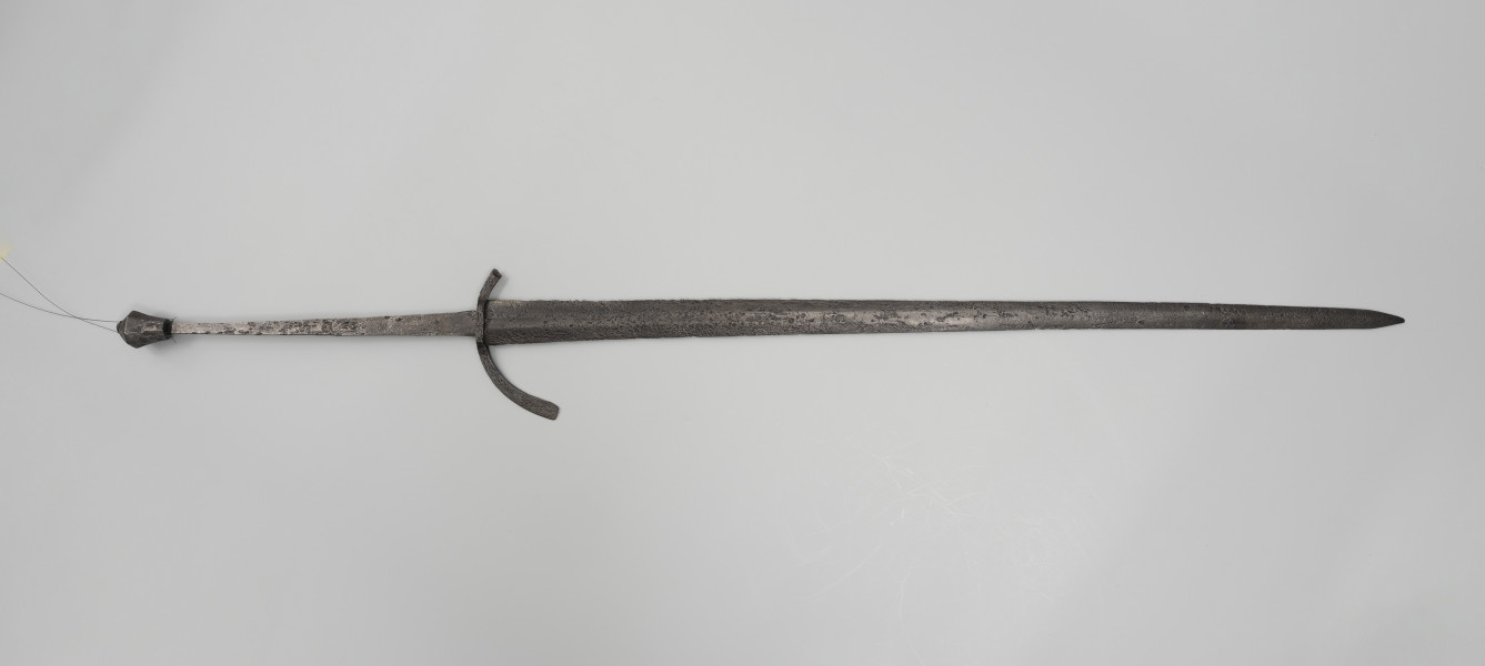Miecz dwuręczny typu XVII (Oakeshott) - ujęcie z przodu; Miecz według typologii Oakeshotta jest typu XVII, T, 9. Głownia zwężająca się ku sztychowi jest dwusieczna, ze zbroczem, a w przekroju romboidalna. Jelec jest wygięty łukiem ku głowni, a z jednej strony ułamany. Pozostałe ramię rozszerzające się na końcu jest o przekroju prostokątnym. Trzpień jest długi, zwężający się ku głowicy i pozwalający uchwycić broń dwiema rękami. Okładzina rękojeści nie zachowała się w tym egzemplarzu. Głowica jest wielościenna, wydłużona ku podstawie.