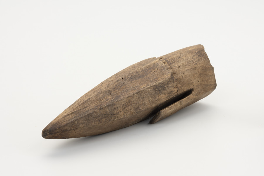 Pochewka na osełkę - ujęcie ze skosu; Pojemnik drewniany do przechowywania osełki z jednego kawałka ﻿drewna. Od górnej części odprowadzony jest uchwyt służący do powieszenia przy pasku w trakcie prac polowych. Na wysokości uchwytu dookolnie wycięte ozdobne ząbki, poniżej których pochwa przybiera stożkowaty kształt.