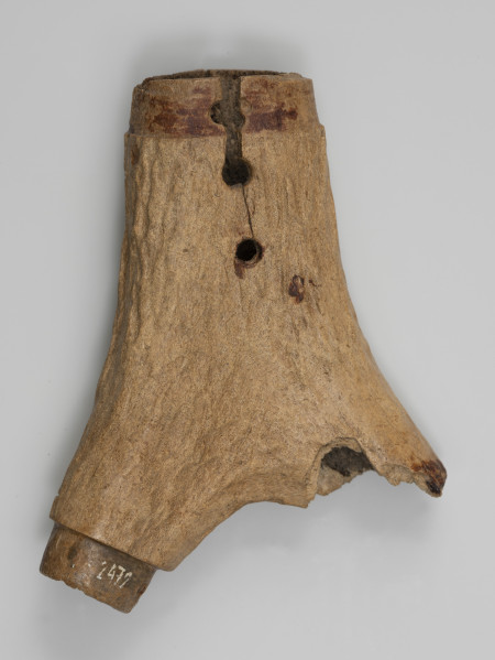 Prochownica - ujęcie z tyłu; Niewielka prochownica z rogu jelenia ma kształt wykorzystujący naturalny wygląd rozwidlenia poroża. Jeden z odrostków jest ułamany, drugi uszkodzony. Metalowe okucia zamykające prochownicę nie zachowały się. Widoczne są trzy otwory, przy jednym z nich jest ubytek masy rogowej, a kolejny z boku przy górnej krawędzi. Prochownica ma naturalną strukturę rogu, lekko wygładzoną.