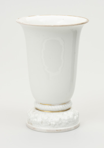 wazon - ujęcie z przodu; Wazon z białej porcelany, rozszerzający się łagodnie, stożkowo od stopy do wylewu, znacznie poszerzonego i lekko wywiniętego na zewnątrz. Krawędź wylewu czary ozdobiona złotym brzegiem - szerokim od strony wewnętrznej na kołnierzu, wąskim od zewnątrz. Miejscami zdobienie wytarte. Podstawa stosunkowo wysoka i ciężka, składa się z niskiego cokolika, ozdobionego złotym paskiem i opartego na nim grubego wałka z plastyczną (wypukłą) dekoracją w formie wieńca kwiatów i liści. Ponad stopą ujęty wklęskami wałek z ornamentem sznurowym. Obie wklęski wypełnione złotym paskiem, uwypuklają zakończenie podstawy i styk z czarą. Podstawa od spodu zagłębiona z uskokiem. Na płaskim dnie stanowiącym spód czary sygnatura wytwórni w kolorze zielonym podszkliwnie, w 2 wierszach: Modell von / Ph.Rosenthal oraz typowy znak firmy - w 2 wierszach Rosenthal (z koroną w środku) / SELB BAVARIA. Na boku podstawy ręcznie zapisany numer 45349 w kolorze brązowym.