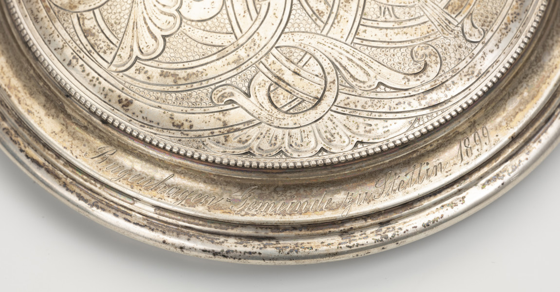 Puszka liturgiczna na komunikanty - detal; Brzeg wieczka ze srebrnymi granulkami. Za nimi ryty kursywą napis w jednej linii: Bugenhagen=Gemeinde zu Stettin 1899.