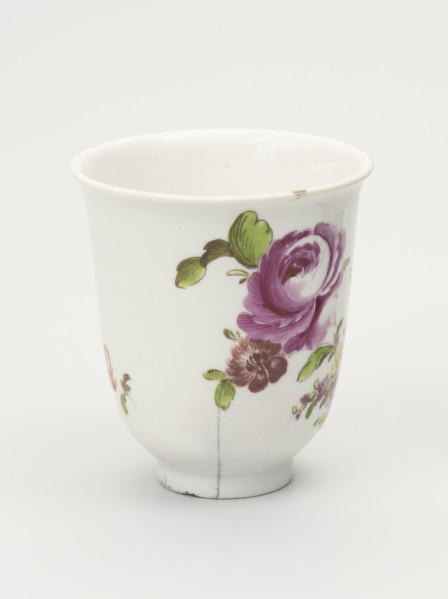 Czarka - ujęcie z boku; Smukła czarka na stopie o dzwonowatej formie z białej porcelany udekorowana malowanymi różnobarwnymi piwoniami. Z prawej duży, pełny, rozwinięty różowy kwiat, poniżej z lewej drobny brązowy kwiat. Wokół drobne zielone liście. U dołu pionowe pęknięcie. U góry na obwodzie widoczny niewielki uszczerbek.