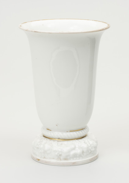 wazon - ujęcie z przodu; Wazon z białej porcelany, rozszerzający się łagodnie, stożkowo od stopy do wylewu, znacznie poszerzonego i lekko wywiniętego na zewnątrz. Krawędź wylewu czary ozdobiona złotym brzegiem - szerokim od strony wewnętrznej na kołnierzu, wąskim od zewnątrz. Podstawa stosunkowo wysoka i ciężka, składa się z niskiego cokolika, ozdobionego złotym paskiem i opartego na nim grubego wałka z plastyczną (wypukłą) dekoracją w formie wieńca kwiatów i liści. Ponad stopą ujęty wklęskami wałek z ornamentem sznurowym. Obie wklęski wypełnione złotym paskiem, uwypuklają zakończenie podstawy i styk z czarą. Podstawa od spodu zagłębiona z uskokiem. Na płaskim dnie stanowiącym spód czary sygnatura wytwórni w kolorze zielonym podszkliwnie, w 2 wierszach: Modell von / Ph.Rosenthal oraz typowy znak firmy - w 2 wierszach Rosenthal (z koroną w środku) / SELB BAVARIA. Na boku podstawy ręcznie zapisany numer 45349 w kolorze brązowym.