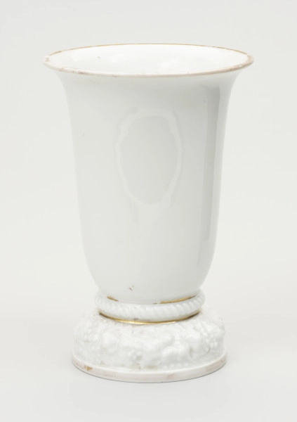 wazon - ujęcie z przodu; Wazon z białej porcelany, rozszerzający się łagodnie, stożkowo od stopy do wylewu, znacznie poszerzonego i lekko wywiniętego na zewnątrz. Krawędź wylewu czary ozdobiona złotym brzegiem - szerokim od strony wewnętrznej na kołnierzu, wąskim od zewnątrz. Podstawa stosunkowo wysoka i ciężka, składa się z niskiego cokolika, ozdobionego złotym paskiem i opartego na nim grubego wałka z plastyczną (wypukłą) dekoracją w formie wieńca kwiatów i liści. Ponad stopą ujęty wklęskami wałek z ornamentem sznurowym. Obie wklęski wypełnione złotym paskiem, uwypuklają zakończenie podstawy i styk z czarą. Podstawa od spodu zagłębiona z uskokiem. Na płaskim dnie stanowiącym spód czary sygnatura wytwórni w kolorze zielonym podszkliwnie, w 2 wierszach: Modell von / Ph.Rosenthal oraz typowy znak firmy - w 2 wierszach Rosenthal (z koroną w środku) / SELB BAVARIA. Na boku podstawy ręcznie zapisany numer 45349 w kolorze brązowym.