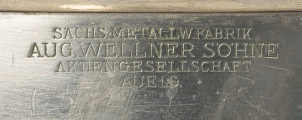 Kubełek do chłodzenia szampana szczecińskiego Knzerthaus - detal; W centrum cylindrycznej części czary napis grawerowany pisanką: SÄCHS. METALLW.FABRIK AUG. WELLNER SÖHNE AKTIENGESELLSCHAFT AUE i.S.