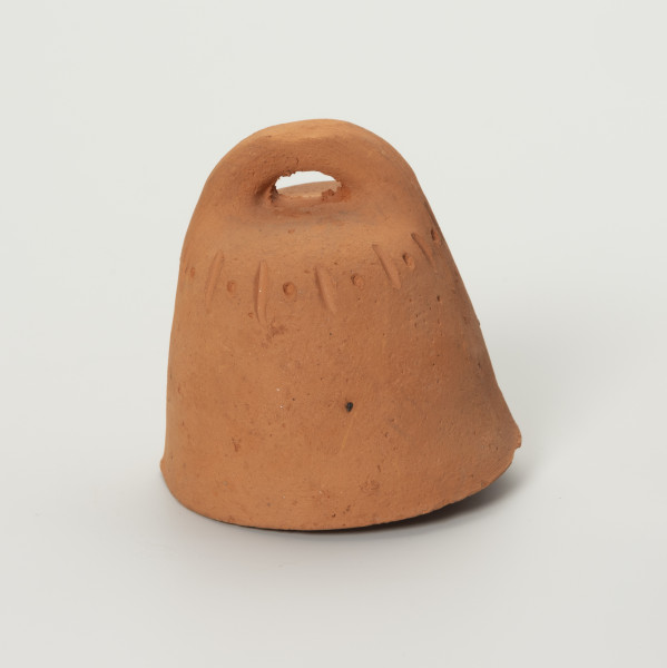 Dzwonek Heleny Kurcyusz - ujęcie z przodu; Gliniany dzwonek kloszowy, bez wyraźnie wyodrębnionego płaszcza i wieńca. Szeroka korona w dwóch przeciwległych miejscach nachodzi na brzegi hełmu i górnej krawędzi. Zdobiony przy krawędzi górnej prostym, dookolnym ornamentem z rytych naprzemiennie pionowych kresek i punktów.