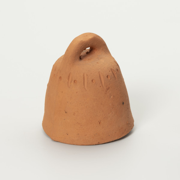 Dzwonek Heleny Kurcyusz - ujęcie z boku; Gliniany dzwonek kloszowy, bez wyraźnie wyodrębnionego płaszcza i wieńca. Szeroka korona w dwóch przeciwległych miejscach nachodzi na brzegi hełmu i górnej krawędzi. Zdobiony przy krawędzi górnej prostym, dookolnym ornamentem z rytych naprzemiennie pionowych kresek i punktów.