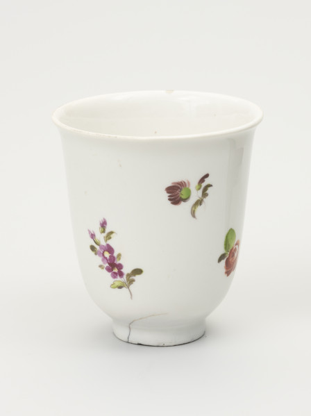 Czarka - ujęcie z przodu; Smukła czarka na stopie o dzwonowatej formie z białej porcelany udekorowana malowanymi różnobarwnymi kwiatami z zielonymi listkami. U dołu niewielkie nieregularne pęknięcie.