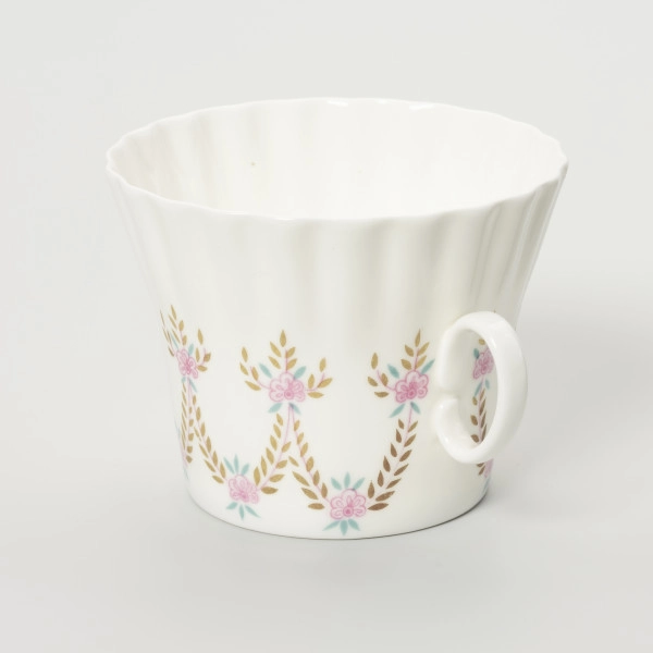 Filiżanka - ujęcie z boku; Duża filiżanka z białej porcelany o lekko dzwonowatej formie, z płaskim dnem i karbowaną górną częścią czarki. Uszko proste, owalne doklejone pośrodku wysokości. Dekorowana malowanymi festonami z wici roślinno-kwiatowej w barwach różu, zieleni i starego złota.