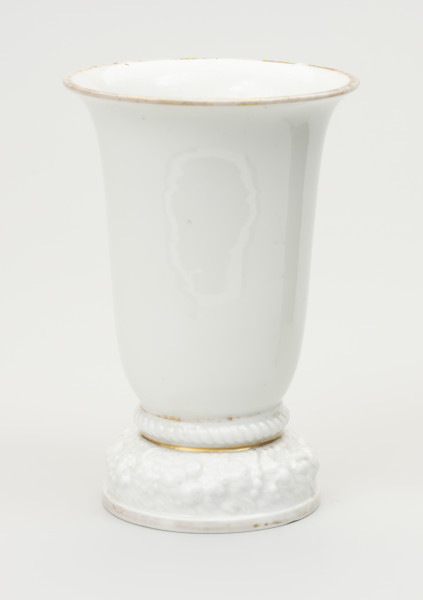 wazon - ujęcie z przodu; Wazon z białej porcelany, rozszerzający się łagodnie, stożkowo od stopy do wylewu, znacznie poszerzonego i lekko wywiniętego na zewnątrz. Krawędź wylewu czary ozdobiona złotym brzegiem - szerokim od strony wewnętrznej na kołnierzu, wąskim od zewnątrz. Miejscami zdobienie wytarte. Podstawa stosunkowo wysoka i ciężka, składa się z niskiego cokolika, ozdobionego złotym paskiem i opartego na nim grubego wałka z plastyczną (wypukłą) dekoracją w formie wieńca kwiatów i liści. Ponad stopą ujęty wklęskami wałek z ornamentem sznurowym. Obie wklęski wypełnione złotym paskiem miejscami wytartym, uwypuklają zakończenie podstawy i styk z czarą. Podstawa od spodu zagłębiona z uskokiem. Na płaskim dnie stanowiącym spód czary sygnatura wytwórni w kolorze zielonym podszkliwnie, w 2 wierszach: Modell von / Ph.Rosenthal oraz typowy znak firmy - w 2 wierszach Rosenthal (z koroną w środku) / SELB BAVARIA. Na boku podstawy ręcznie zapisany numer 45349 w kolorze brązowym.