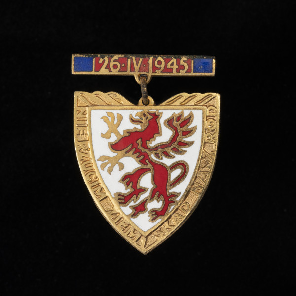 Odznaka Gryfa Pomorskiego - ujęcie z przodu; Metalowa pozłacana i emaliowana odznaka w formie tarczy piastowskiej na zawieszce. Na awersie na białej emaliowanej tarczy herbowej przedstawiony jest czerwony, stojący gryf pomorski. Na pozłacanych brzegach tarczy napis: NIE RZUCIM ZIEMI SKĄD NASZ RÓD. Odznaka zawieszona jest na zawieszce metalowej emaliowanej na czerwono z granatowymi paskami wzdłuż bocznych krawędzi. Na czerwonej emalii umieszczono datę: 26•IV•1945.