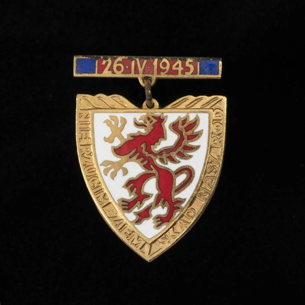 Odznaka Gryfa Pomorskiego - ujęcie z przodu; Metalowa pozłacana i emaliowana odznaka w formie tarczy piastowskiej na zawieszce. Na awersie na białej emaliowanej tarczy herbowej przedstawiony jest czerwony, stojący gryf pomorski. Na pozłacanych brzegach tarczy napis: NIE RZUCIM ZIEMI SKĄD NASZ RÓD. Odznaka zawieszona jest na zawieszce metalowej emaliowanej na czerwono z granatowymi paskami wzdłuż bocznych krawędzi. Na czerwonej emalii umieszczono datę: 26•IV•1945.