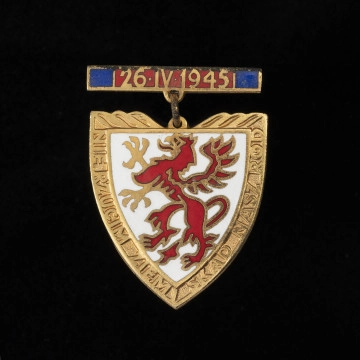 Odznaka Gryfa Pomorskiego - ujęcie z przodu; Metalowa pozłacana i emaliowana odznaka w formie tarczy piastowskiej na zawieszce. Na awersie na białej emaliowanej tarczy herbowej przedstawiony jest czerwony, stojący gryf pomorski. Na pozłacanych brzegach tarczy napis: NIE RZUCIM ZIEMI SKĄD NASZ RÓD. Odznaka zawieszona jest na zawieszce metalowej emaliowanej na czerwono z granatowymi paskami wzdłuż bocznych krawędzi. Na czerwonej emalii umieszczono datę: 26•IV•1945.