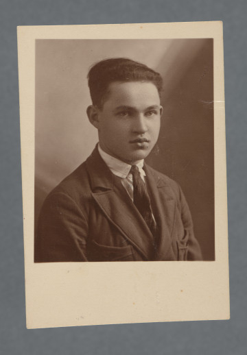 Fotograficzne popiersie młodego mężczyzny o zaczesanych do tyłu włosach, Mordki (Józefa) Englendera; twarz ujęta w trzech czwartych, koszula w paski z czarnym krawatem, nieco jaśniejsza od krawata marynarka. Fotografia monochromatyczna, w sepii, z szerokim marginesem u dołu, odbitka podłużnie prostokątna, samo zdjęcie - zbliżone do kwadratu (krawędzie boczne nieco dłuższe od dolnej i górnej). Krawędzie proste. Przy krawędzi dłuższej rewersu nr piórem - zakładu fot.? - 11189