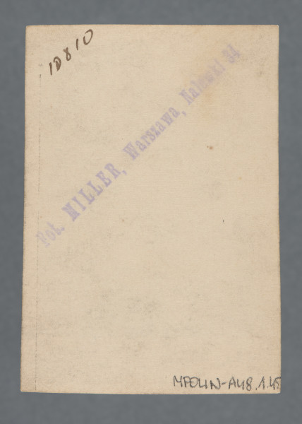 Fotografia monochromatyczna, w sepii, przedstawia uśmiechniętego młodego mężczyznę, tego samego i zapewne w tej samej marynarce i koszuli co na zdjęciu wcześniejszym, w klapie marynarki nie ma jednak, w odróżnieniu od tamtego, przypinki.Kołnierzyk - duży - białej koszuli wyłożony na ciemną (nie czarną) marynarkę.Pieczątka zakładu fotograficznego pozwala domniemywać, że zdjęcie nie zostało wykonane przed 1930 - w kolekcji znajdują się zdjęcia z dedykacjami z różnych okresów, wywołanych w tym zakładzie - niektóre zdjęcia z dedykacjami z 1930 r. i wcześniejszymi mają jeszcze inną pieczątkę firmową.Krawędzie proste, wzdłuż których jasny margines, większy u dołu.W lewym górnym rogu rewersu widoczny nr czarnym piórem: 13[?]810 - skośnie. rewers z zabrudzeniem.