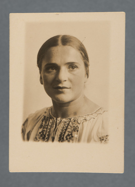 Fotografia portretowa Mani Żelaznej, uczesanej z przedziałkiem, ubranej w białą koszulę z haftem ludowym. Popiersie, twarz w trzech czwartych. Zapewne z okresu, kiedy wyjeżdżała albo niedługo po tym, jak wyjechała z Polski.Krawędzie proste, zdjęcie obramowane marginesem, największym u dołu.W lewym górnym rogu rewersu widoczny odcisk czyjegoś palca.