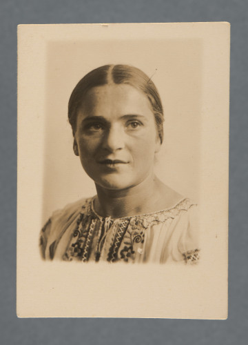 Fotografia portretowa Mani Żelaznej, uczesanej z przedziałkiem, ubranej w białą koszulę z haftem ludowym. Popiersie, twarz w trzech czwartych. Zapewne z okresu, kiedy wyjeżdżała albo niedługo po tym, jak wyjechała z Polski.Krawędzie proste, zdjęcie obramowane marginesem, największym u dołu.W lewym górnym rogu rewersu widoczny odcisk czyjegoś palca.