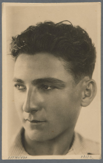 Fotografia portretowa młodego mężczyzny, półprofil, patrzy w lewo - część twarzy mniej widoczna mocno oświetlona, co nadaje zdjęciu charakter artystyczny; ciemne niedługie włosy postawione do góry. Widoczna prążkowana jasna koszula. Zdjęcie wywołane na papierze z nadrukiem pocztówkowym. Krawędzie odbitki proste, widoczny jest wzdłuż nich margines.