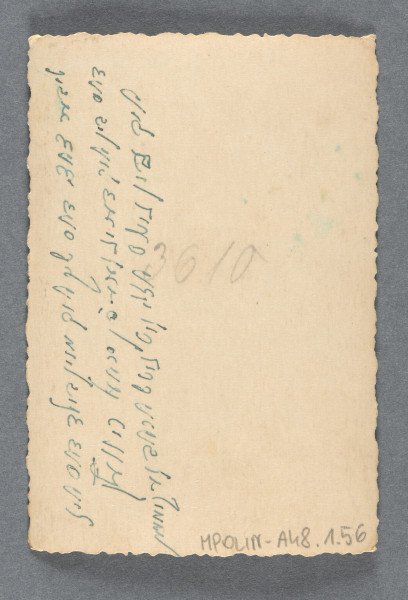 Fotografia nastoletniego chłopca w grubej czapce z daszkiem i samym garniturze i koszuli, stojącego na śniegu, ujętego na wprost, en face, uśmiechniętego. Stoi na tle ogrodzenia (płot na podmurówce) przed zabudowaniem. Na rewersie widoczny, pod dedykacją, numer - ołówkiem: 3610 Krawędzie odbitki ząbkowane, wzdłuż nich margines.